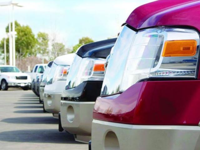 A row of parked trucks in various colors, viewed from the front, on a sunny day.
