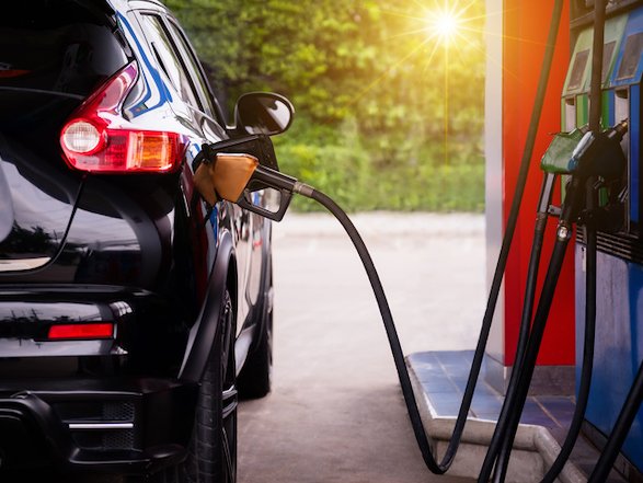 A black car is refueling at a gas station under bright sunlight.