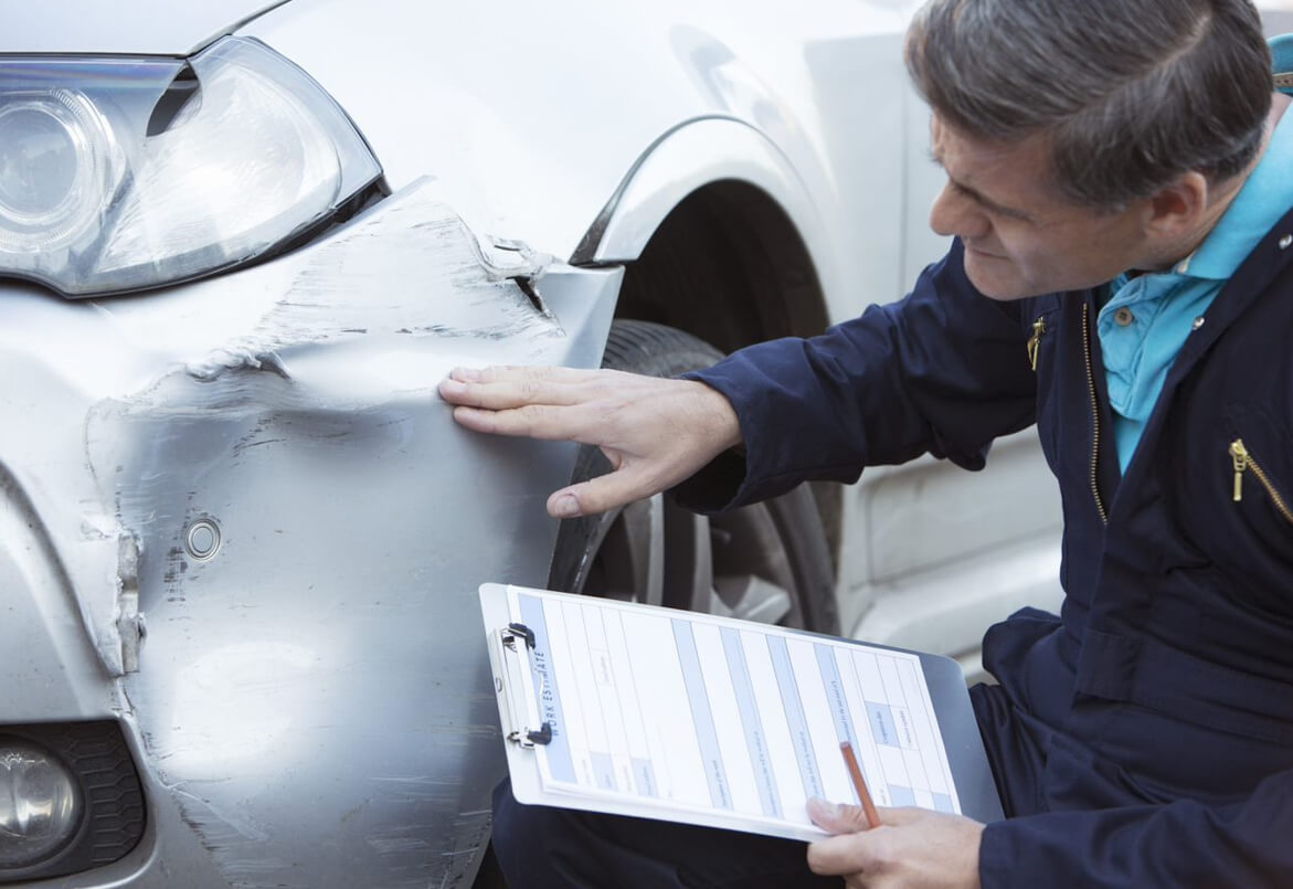 Man inspecting a car's damaged bumper with a clipboard and pen.