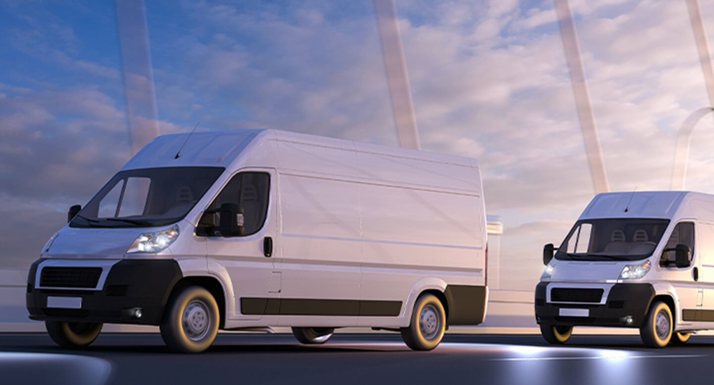Two white delivery vans driving on a road with a cloudy sky in the background.